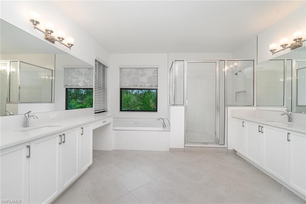 Full bathroom featuring two vanities, a garden tub, a shower stall, and light tile patterned floors