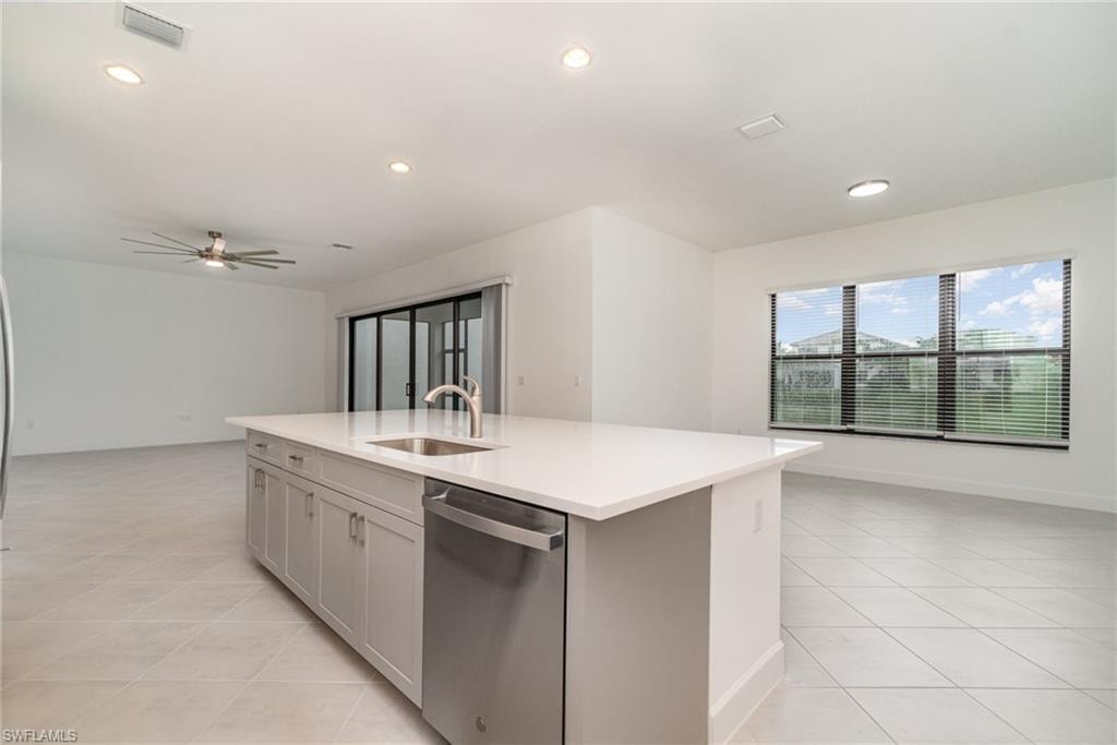 Kitchen featuring open floor plan, stainless steel dishwasher, an island with sink, ceiling fan, and light stone countertops