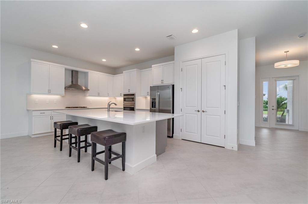 Kitchen featuring white cabinets, stainless steel appliances, a kitchen bar, an island with sink, and light tile patterned floors