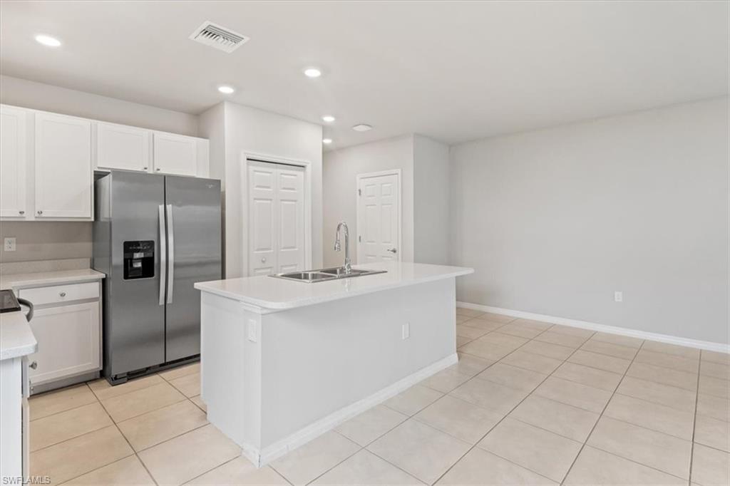 Kitchen with stainless steel fridge, an island with sink, white cabinets, light tile patterned floors, and recessed lighting