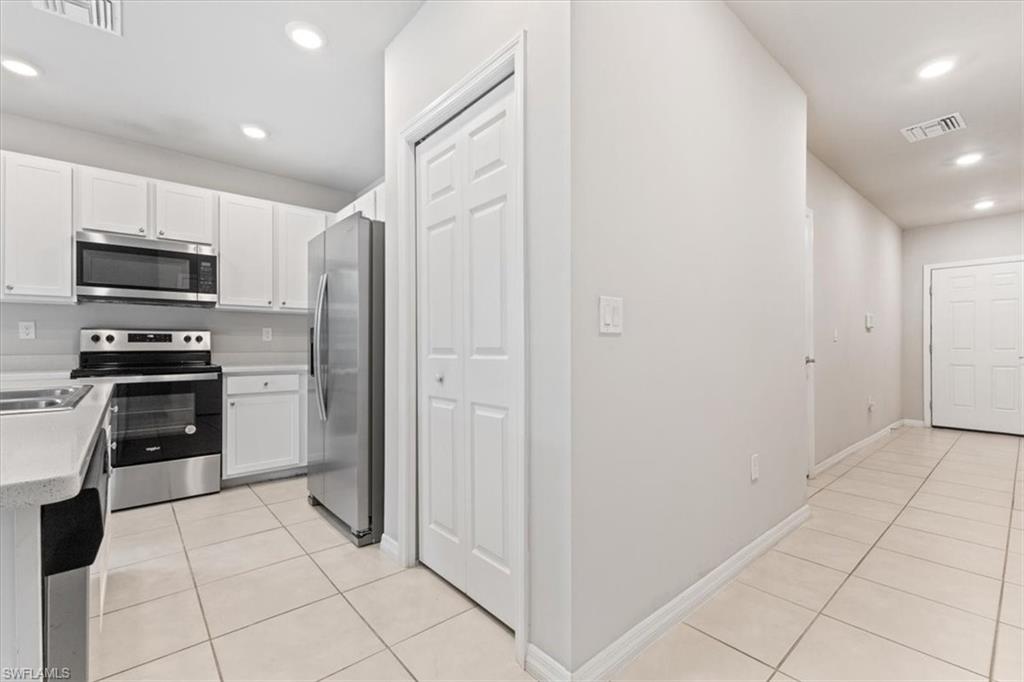 Kitchen with recessed lighting, stainless steel appliances, light tile patterned floors, white cabinets, and light stone countertops