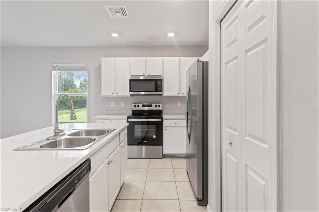 Kitchen with stainless steel appliances, white cabinets, light tile patterned flooring, and recessed lighting