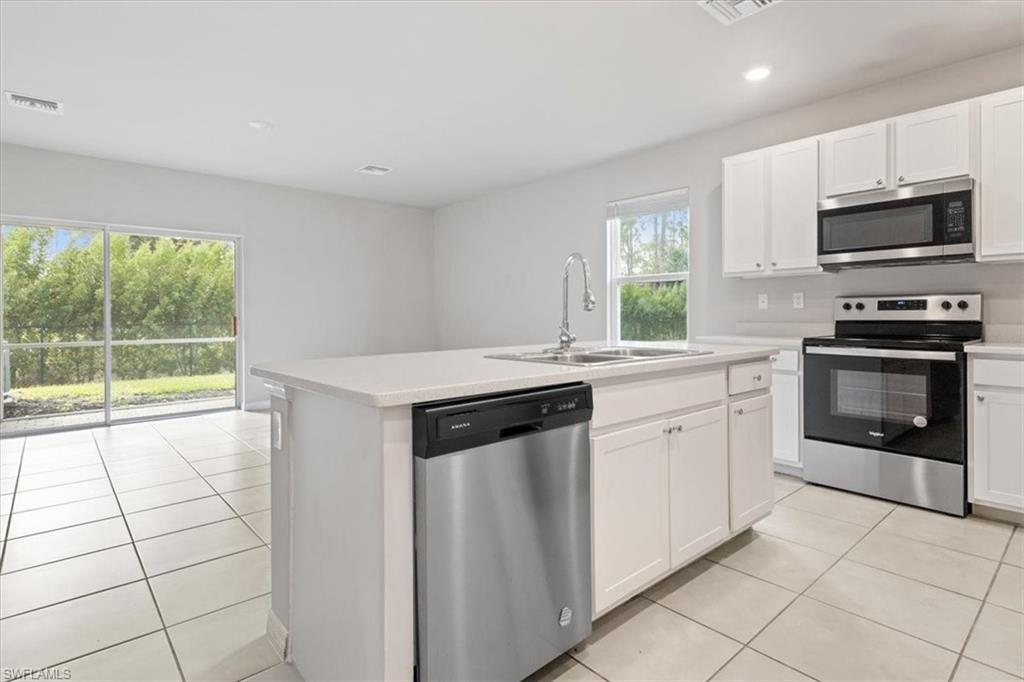 Kitchen featuring stainless steel appliances, light tile patterned flooring, white cabinets, a kitchen island with sink, and recessed lighting