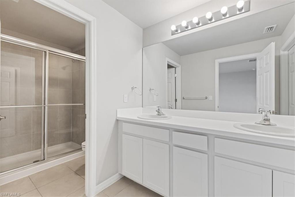 Full bathroom featuring double vanity, a shower stall, and light tile patterned floors