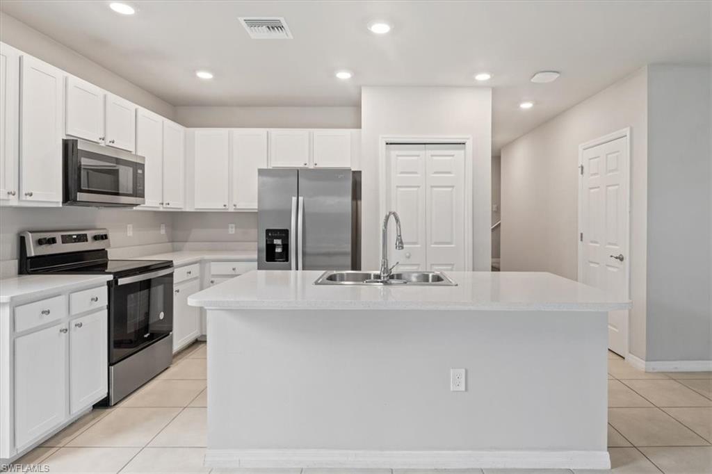 Kitchen with stainless steel appliances, a center island with sink, white cabinets, light tile patterned floors, and recessed lighting