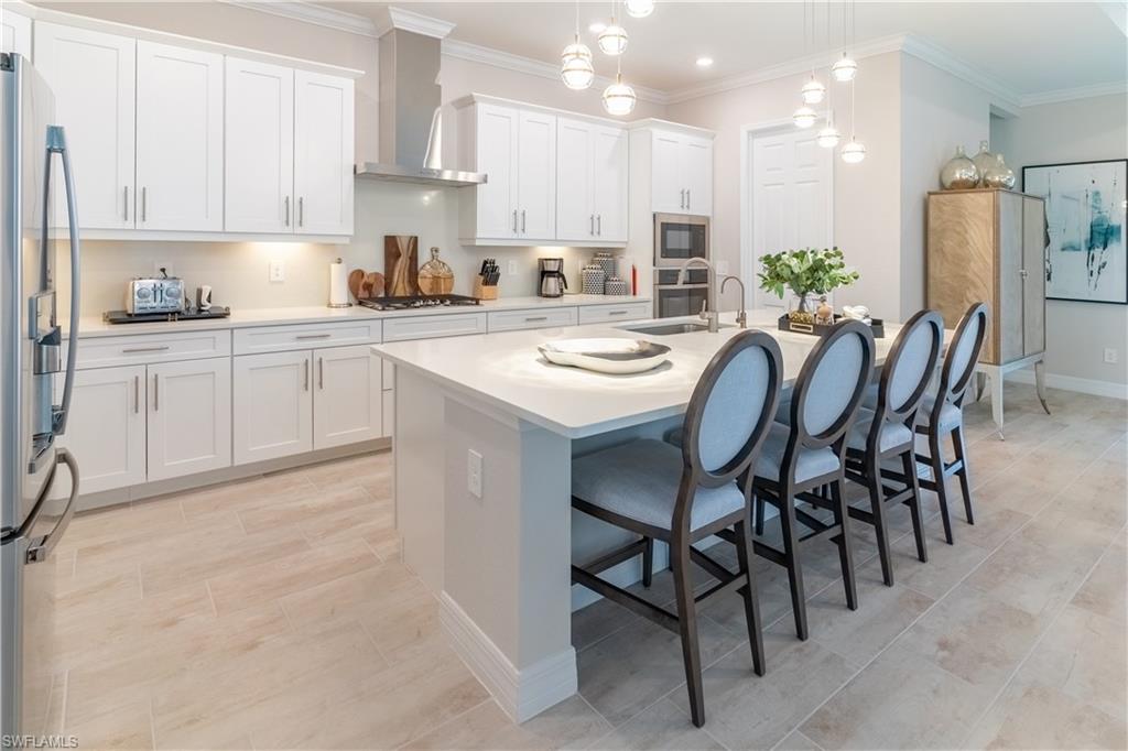Kitchen with decorative light fixtures, wall chimney range hood, stainless steel appliances, a kitchen island with sink, and white cabinets