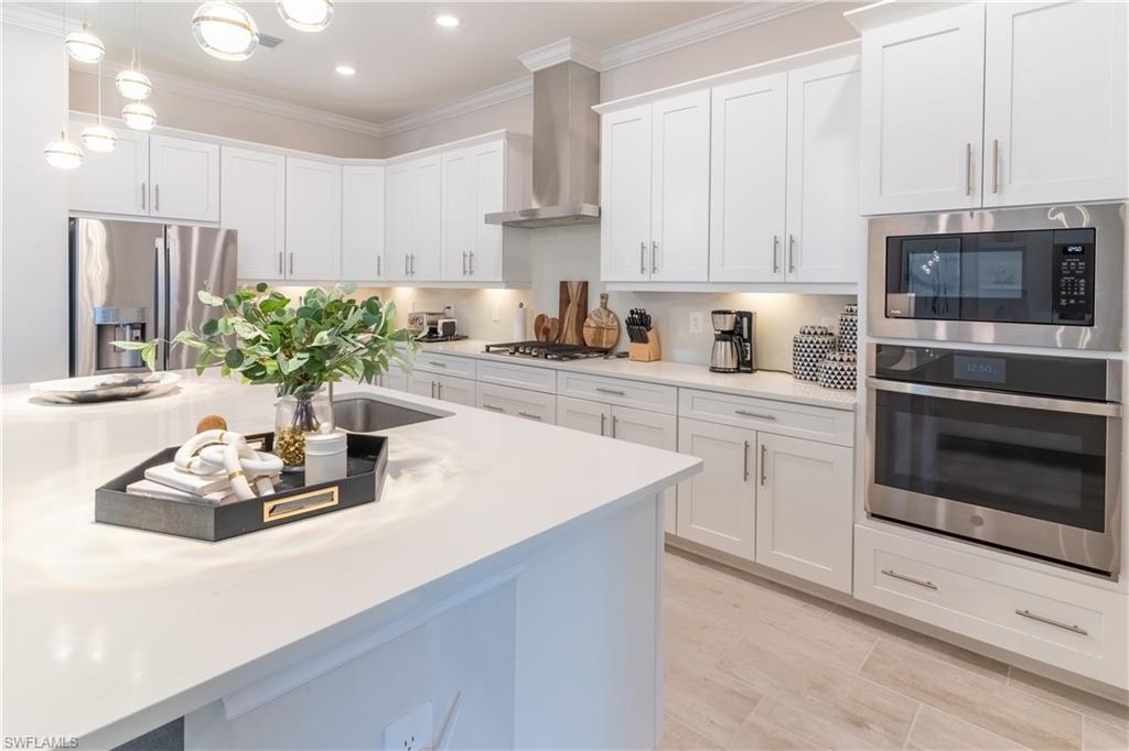 Kitchen with wall chimney exhaust hood, white cabinetry, appliances with stainless steel finishes, and pendant lighting
