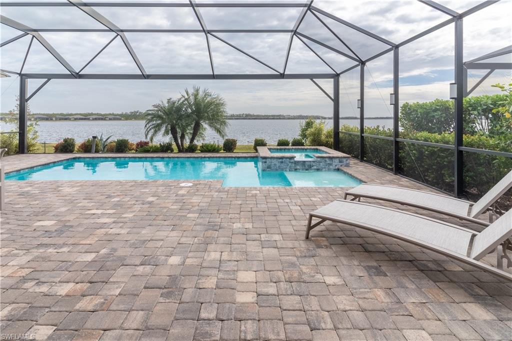 View of pool featuring a patio, an in ground hot tub, a water view, and glass enclosure