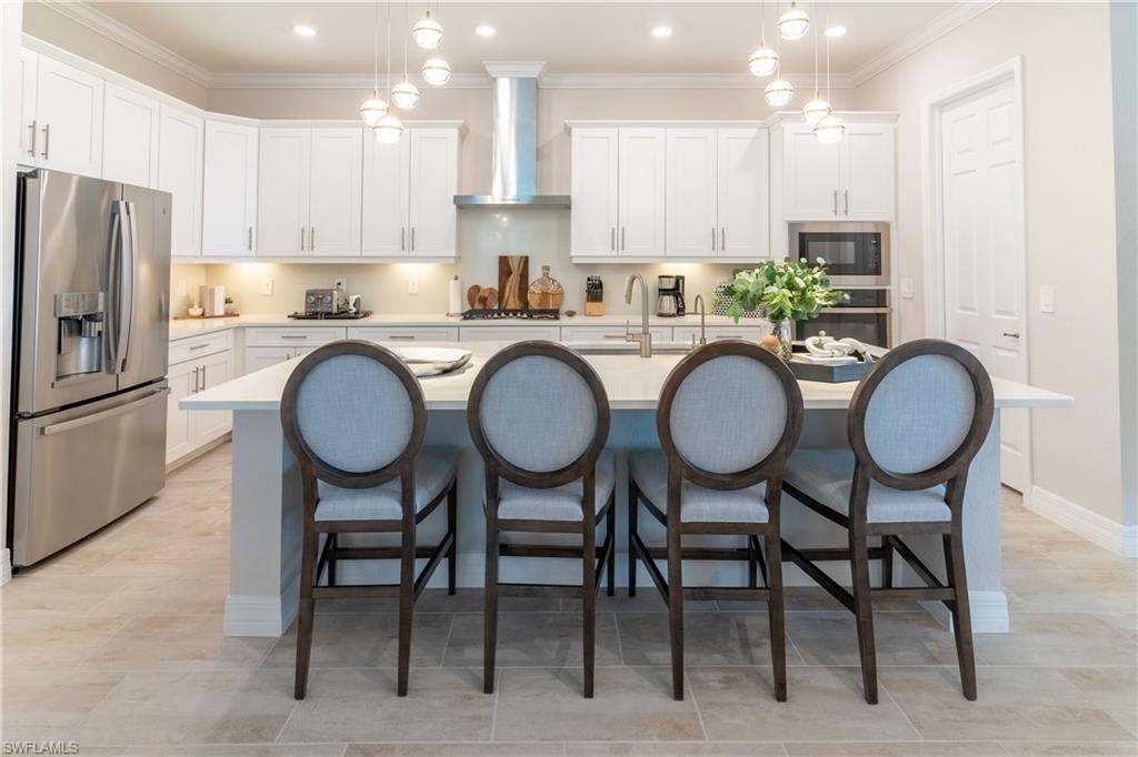 Kitchen featuring decorative light fixtures, white cabinets, a kitchen island with sink, stainless steel appliances, and wall chimney exhaust hood