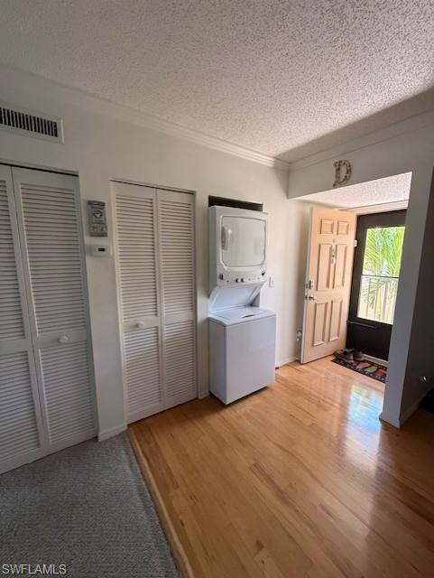 Laundry area with stacked washing machine and dryer, a textured ceiling, light wood-style floors, and ornamental molding