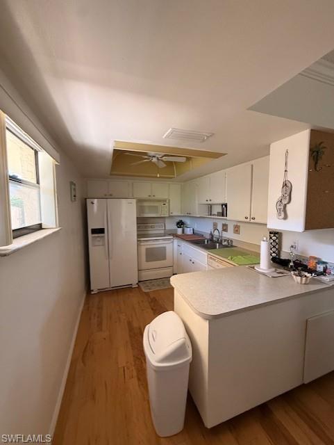 Kitchen featuring white appliances, light countertops, light wood-type flooring, a peninsula, and a ceiling fan