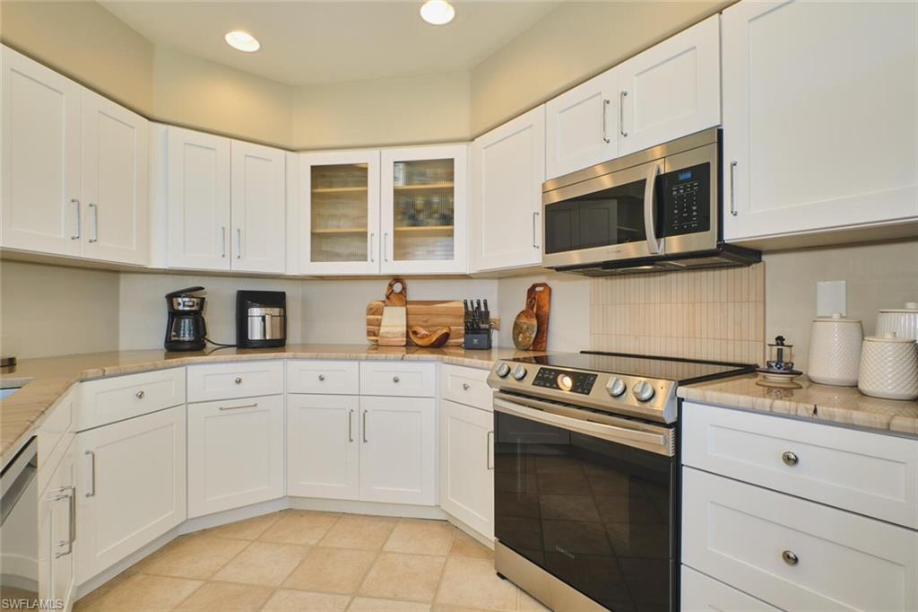 Kitchen featuring stainless steel appliances, white cabinets, glass fronted cabinets, light stone countertops, and recessed lighting
