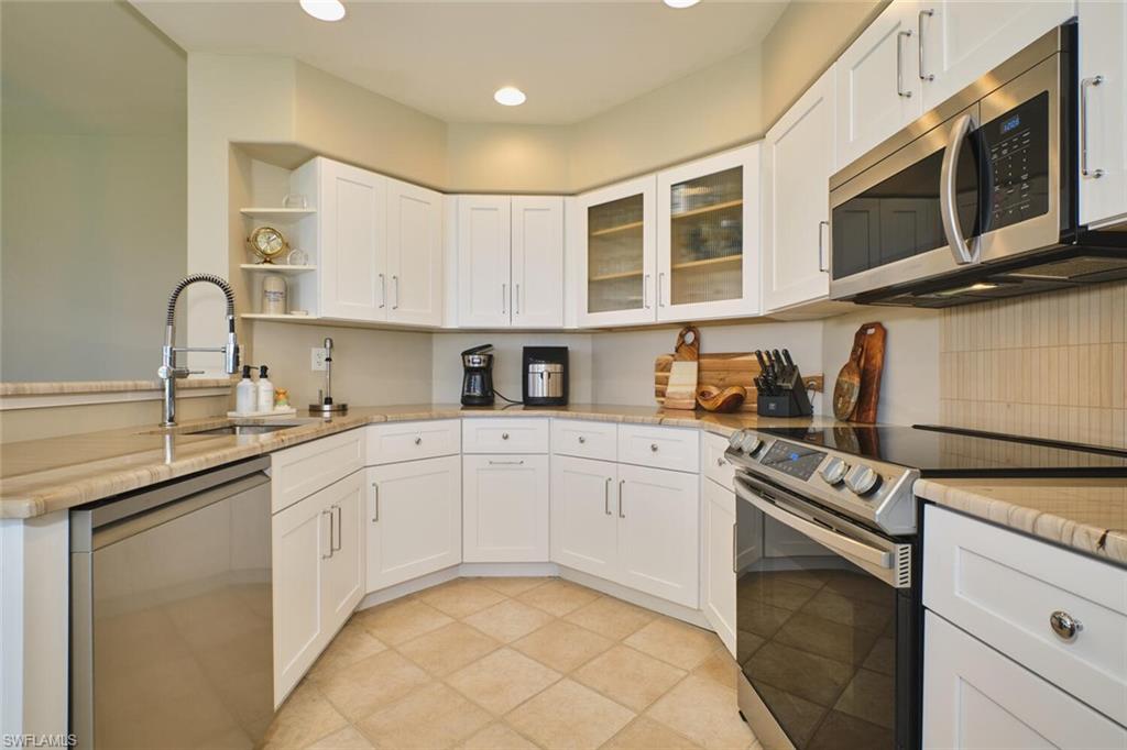 Kitchen featuring stainless steel appliances, white cabinets, light stone counters, glass insert cabinets, and recessed lighting