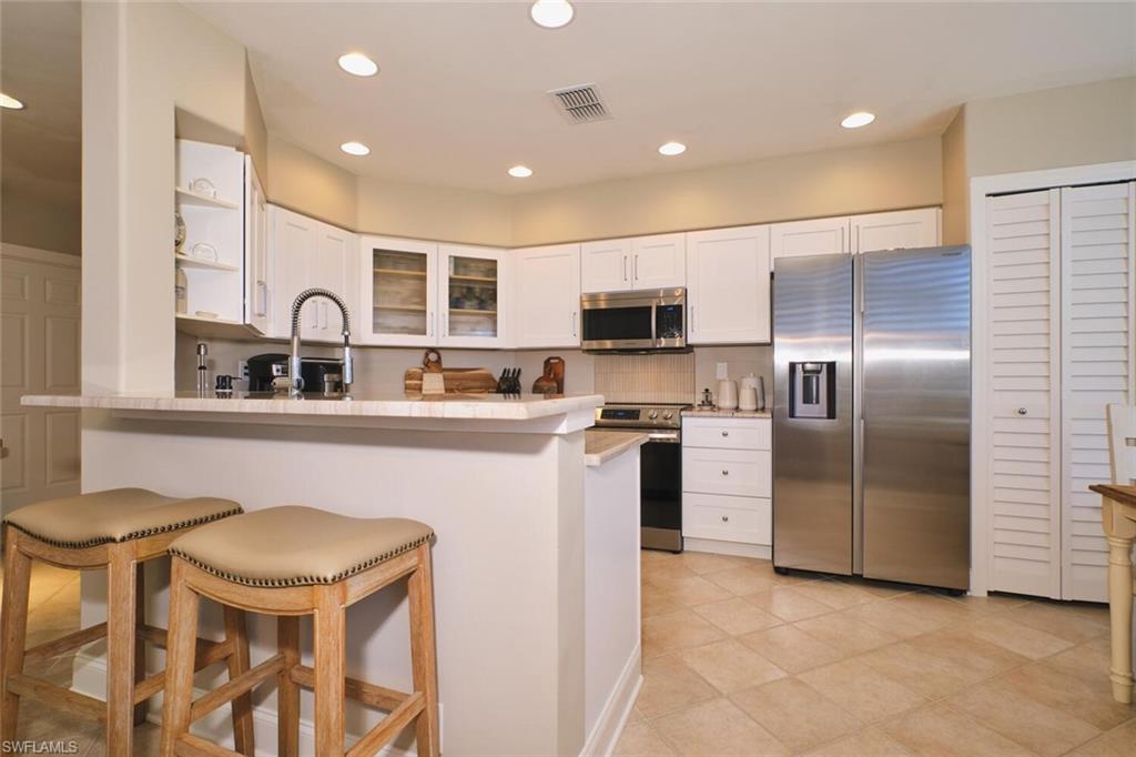 Kitchen with stainless steel appliances, glass fronted cabinets, recessed lighting, a peninsula, and a kitchen breakfast bar