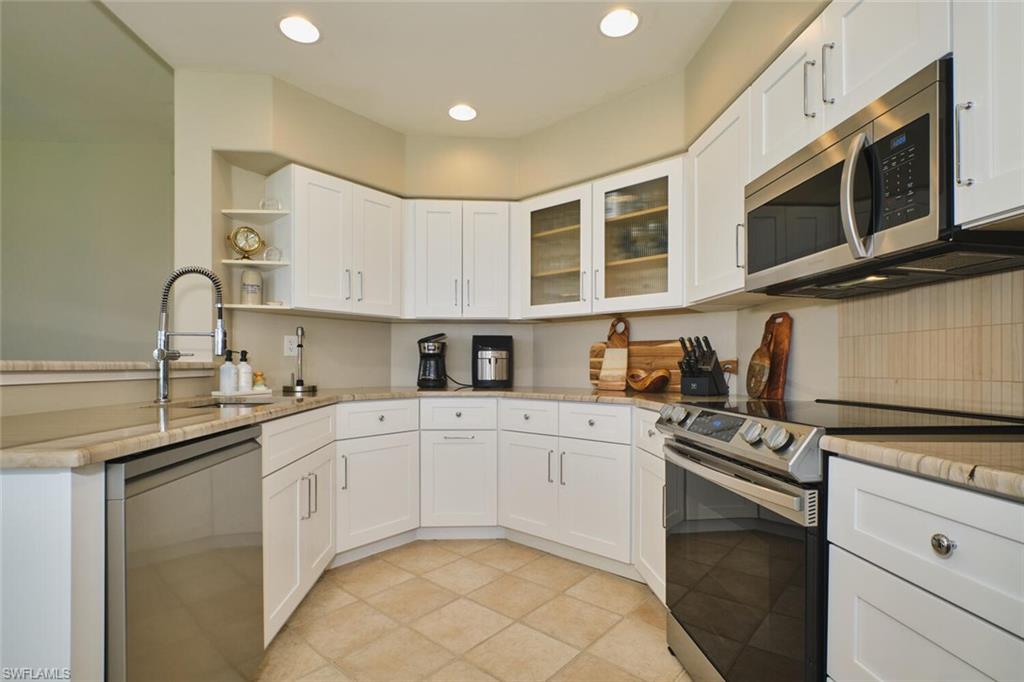 Kitchen featuring stainless steel appliances, white cabinetry, light stone counters, glass fronted cabinets, and recessed lighting
