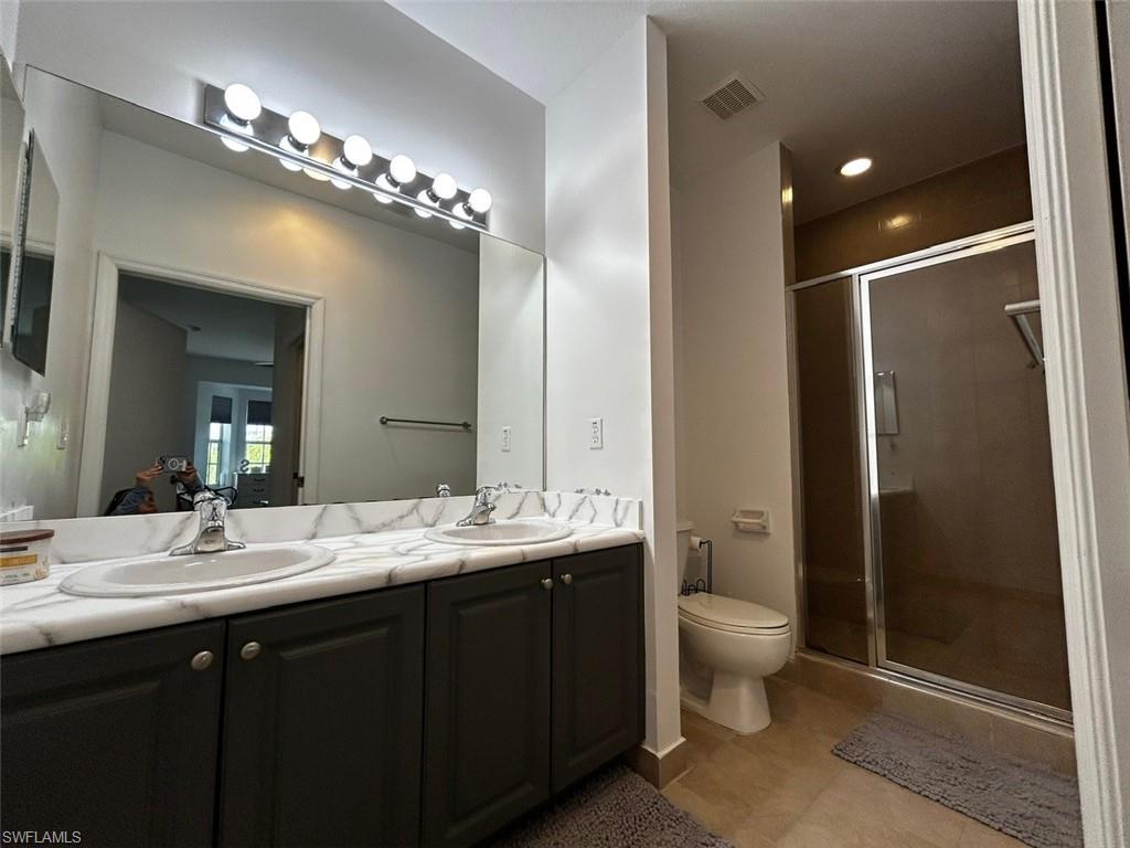 Bathroom featuring double vanity, a shower stall, and light tile patterned floors