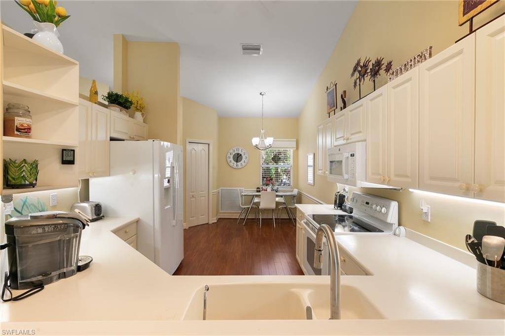 Kitchen with white appliances, dark wood-style floors, open shelves, light countertops, and vaulted ceiling