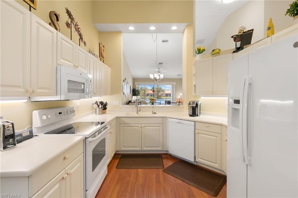 Kitchen with white appliances, light countertops, white cabinetry, dark wood-style flooring, and vaulted ceiling
