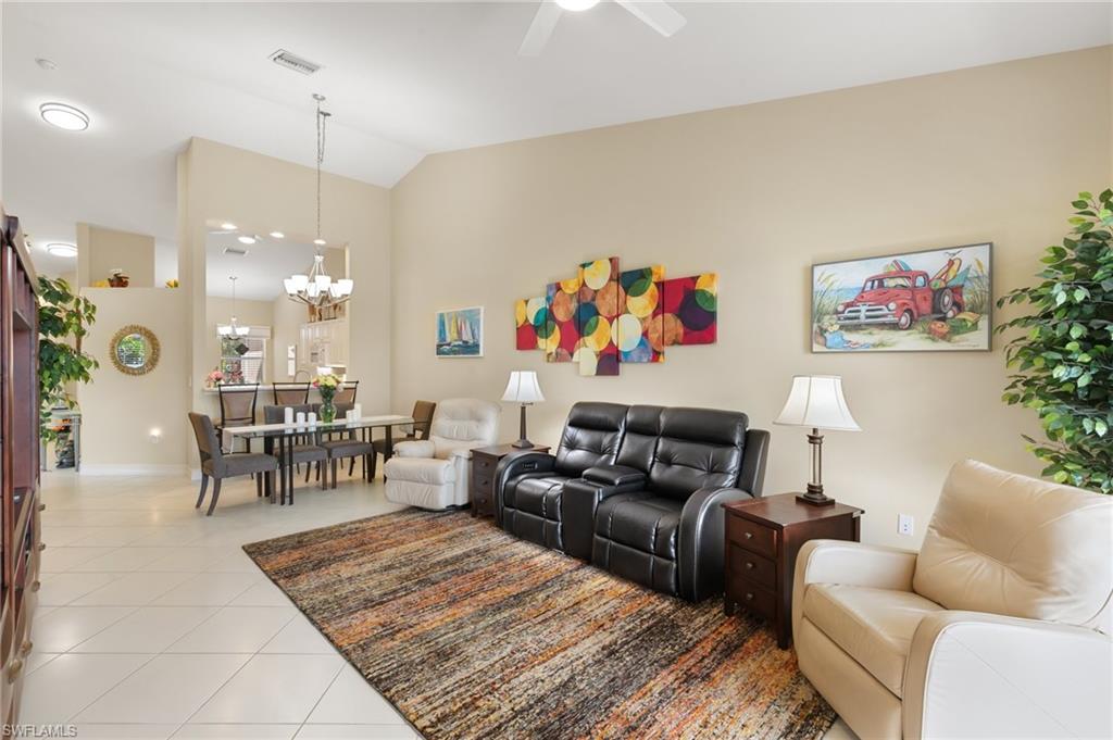 Living area featuring light tile patterned flooring, lofted ceiling, hanging lights, and ceiling fan
