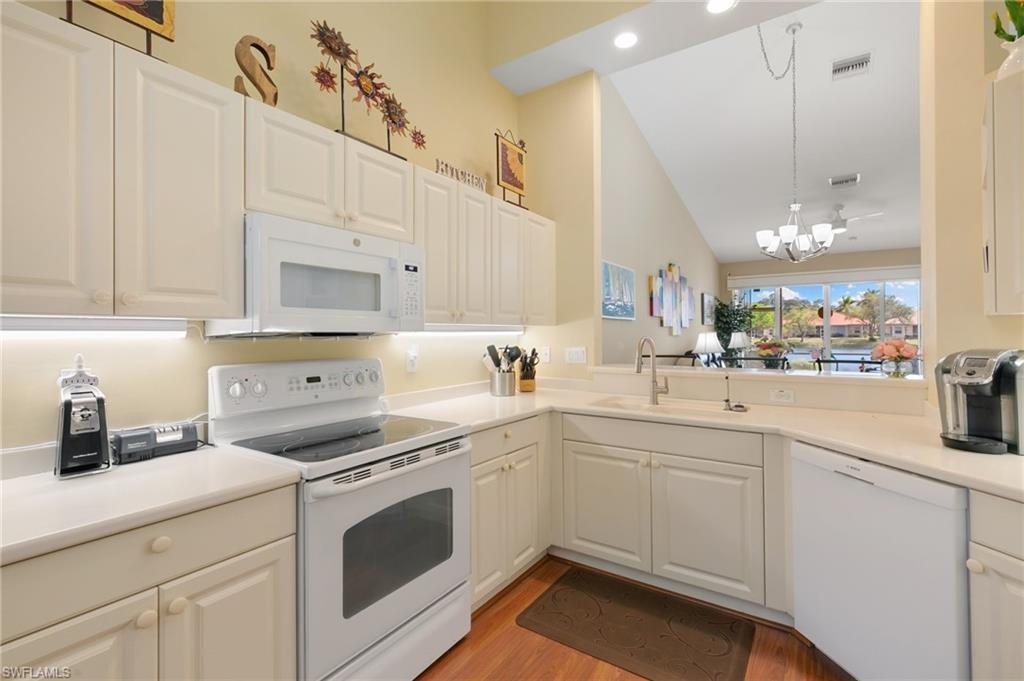 Kitchen featuring white appliances, light countertops, vaulted ceiling, white cabinetry, and light wood-style flooring