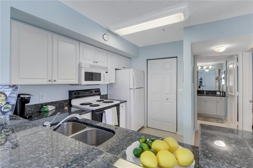 Kitchen featuring electric range oven, white cabinets, white microwave, dark stone countertops, and a textured ceiling