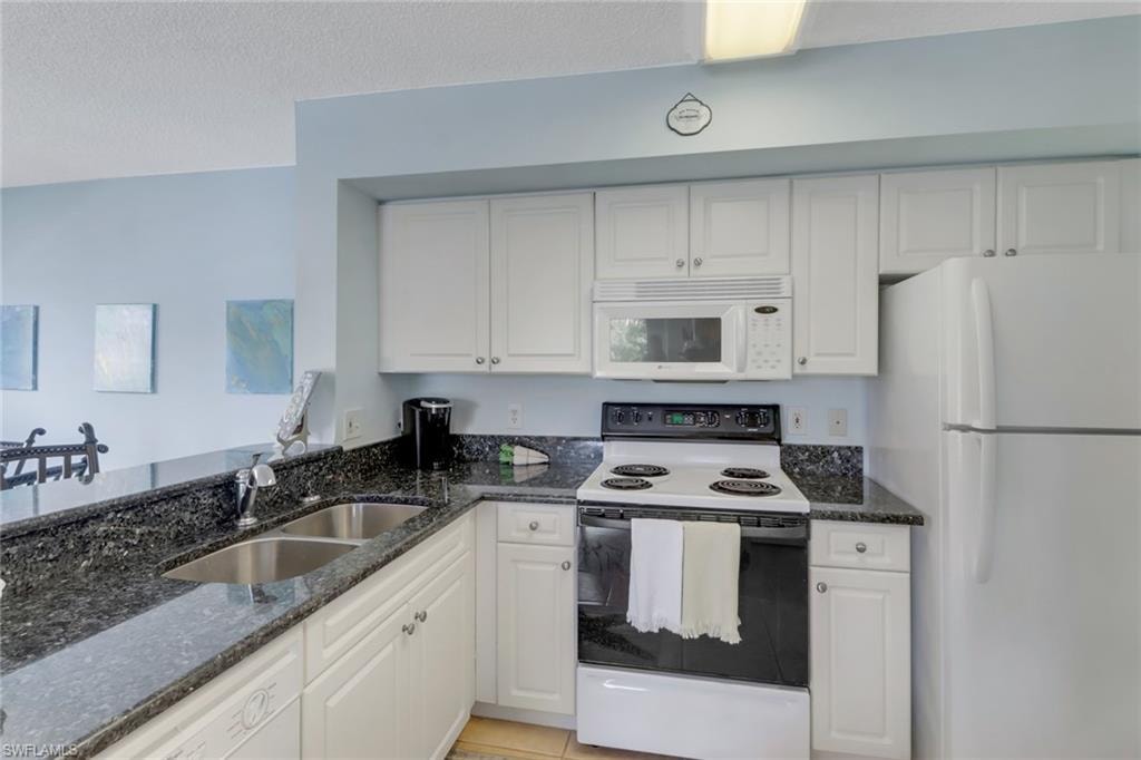 Kitchen with white appliances, white cabinetry, dark stone counters, and a textured ceiling