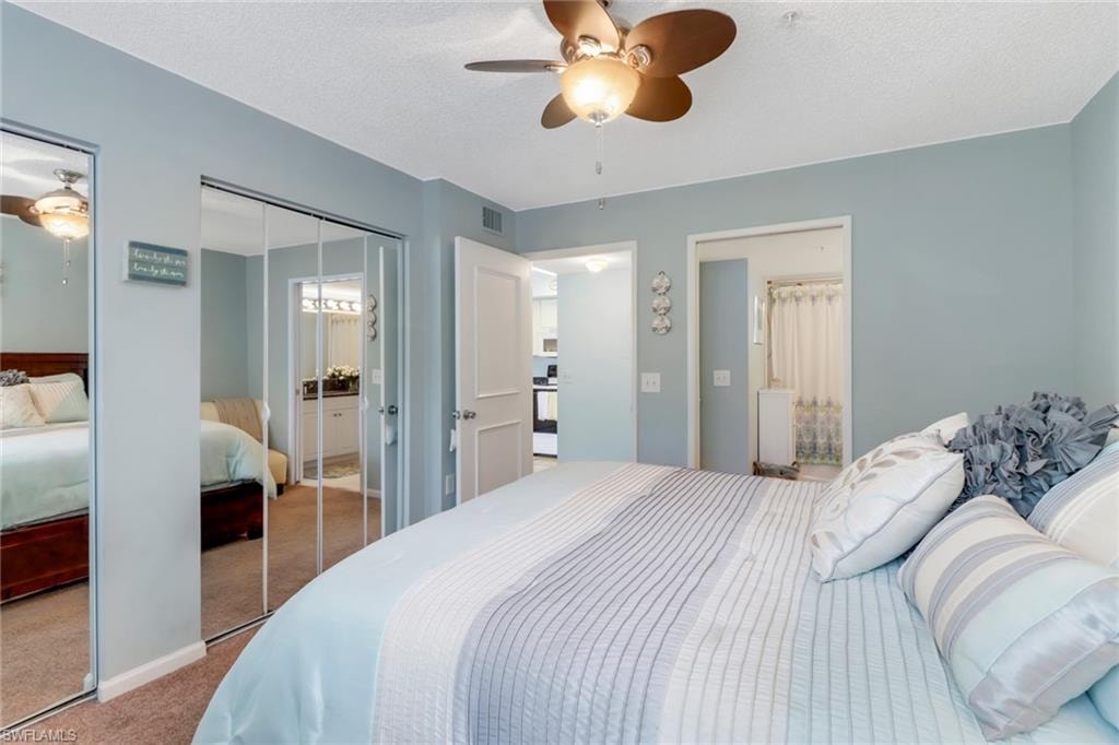 Carpeted bedroom with two closets, ceiling fan, and a textured ceiling
