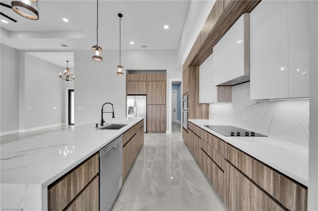 Kitchen with light stone counters, modern cabinets, suspended lighting, dual tone cabinetry, and stainless steel appliances