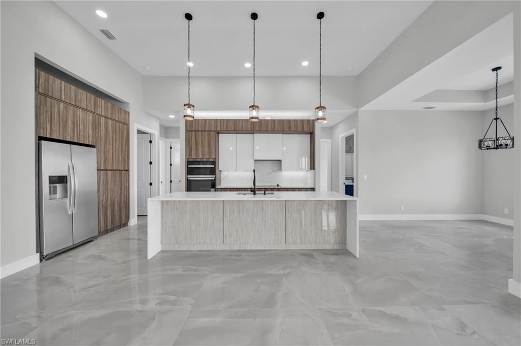 Kitchen featuring stainless steel fridge with ice dispenser, pendant lighting, a large island, modern cabinets, and a high ceiling