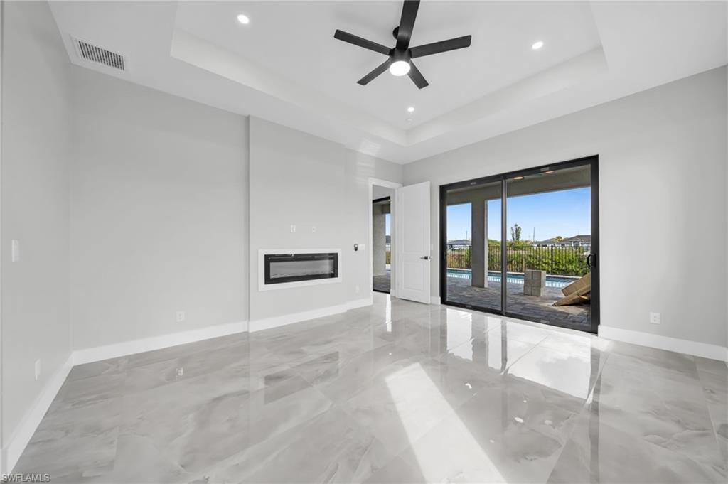 Unfurnished living room with a glass covered fireplace, a ceiling fan, a raised ceiling, and recessed lighting