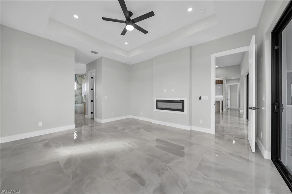 Unfurnished living room with a glass covered fireplace, ceiling fan, recessed lighting, and a tray ceiling