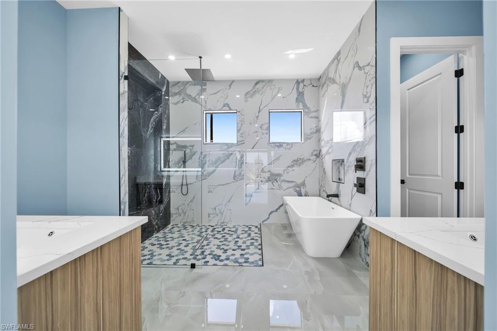 Bathroom with vanity, a marble finish shower, a freestanding bath, and recessed lighting