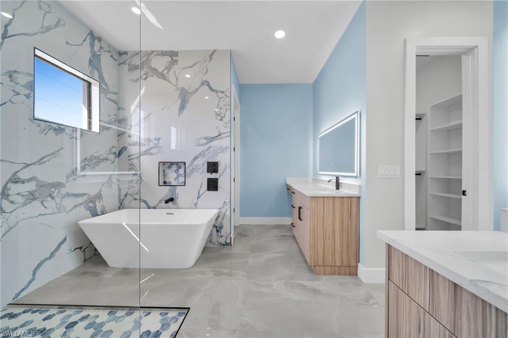 Full bath featuring two vanities, a freestanding bath, recessed lighting, stone wall, and a marble finish shower