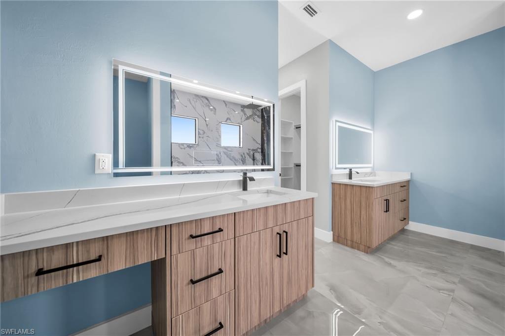Bathroom featuring two vanities, a marble finish shower, and light marble finish floors