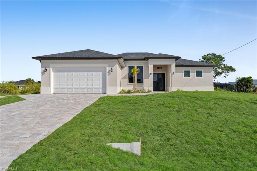 Prairie-style house with stucco siding, decorative driveway, a garage, and a front lawn