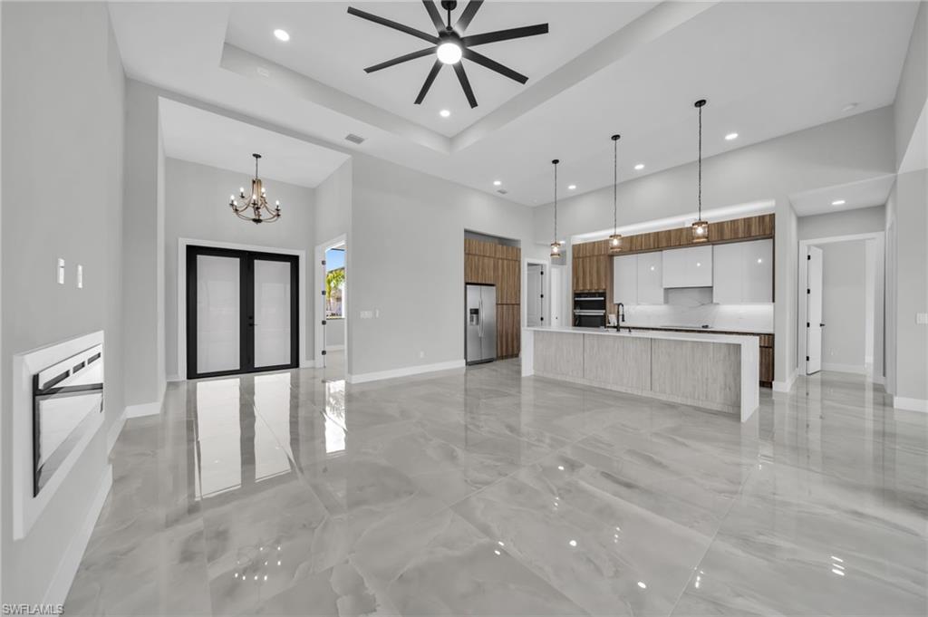 Unfurnished living room with a ceiling fan, a tray ceiling, light marble finish flooring, a chandelier, and french doors