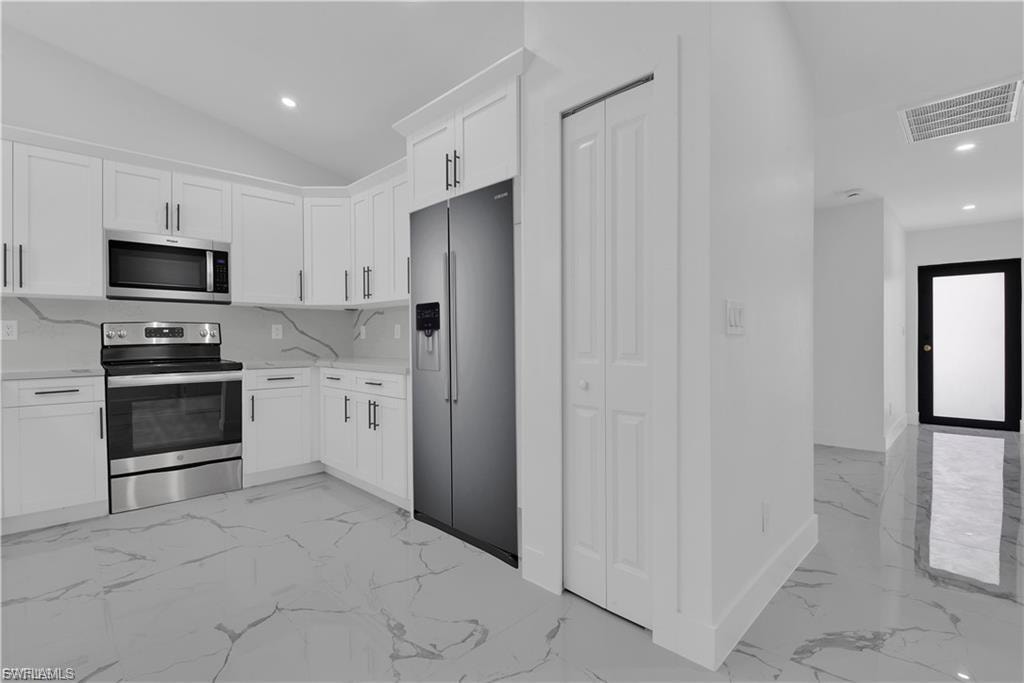 Kitchen with stainless steel appliances, white cabinets, recessed lighting, light marble finish flooring, and light stone countertops