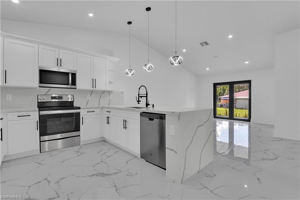 Kitchen featuring stainless steel appliances, light stone countertops, a peninsula, white cabinets, and vaulted ceiling