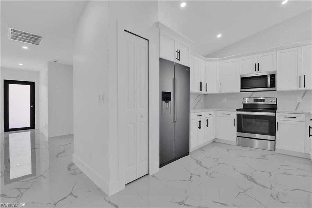 Kitchen featuring stainless steel appliances, recessed lighting, white cabinets, light stone countertops, and vaulted ceiling