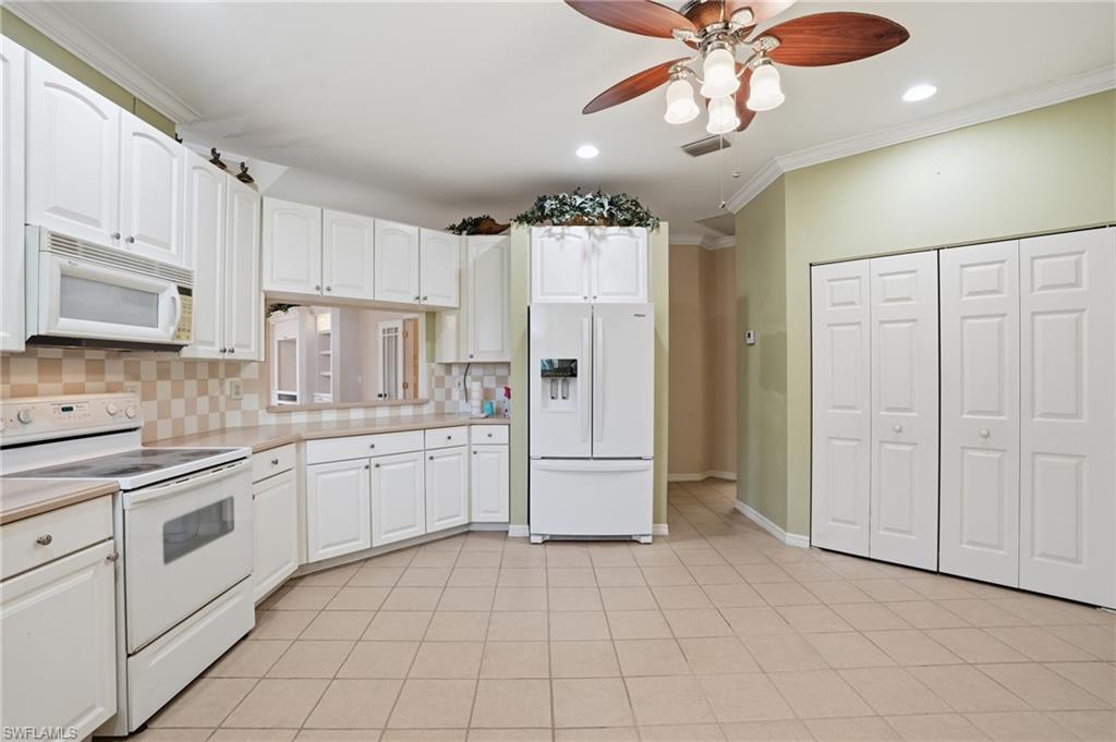 Kitchen with white appliances, a ceiling fan, light countertops, white cabinets, and crown molding - Virtually Edited Image