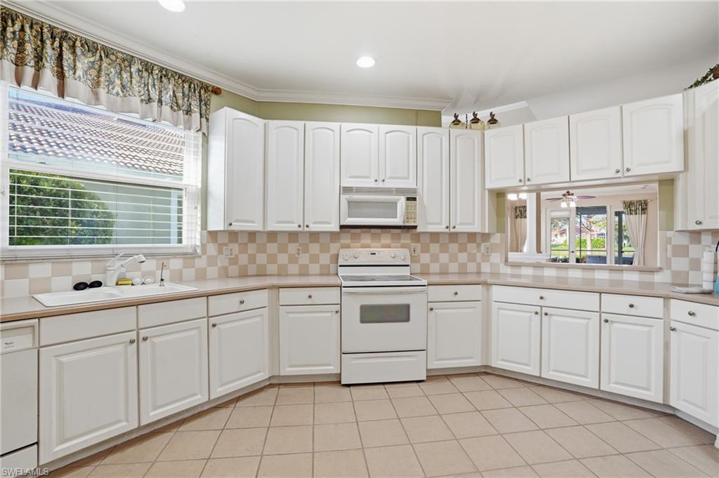 Kitchen with white appliances, white cabinetry, plenty of natural light, light countertops, and recessed lighting - Virtually Edited Image