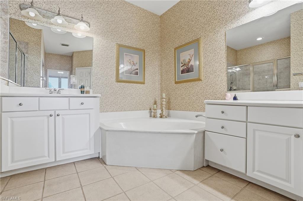 Bathroom featuring two vanities, a garden tub, a stall shower, light tile patterned floors, and wallpapered walls - Virtually Edited Image