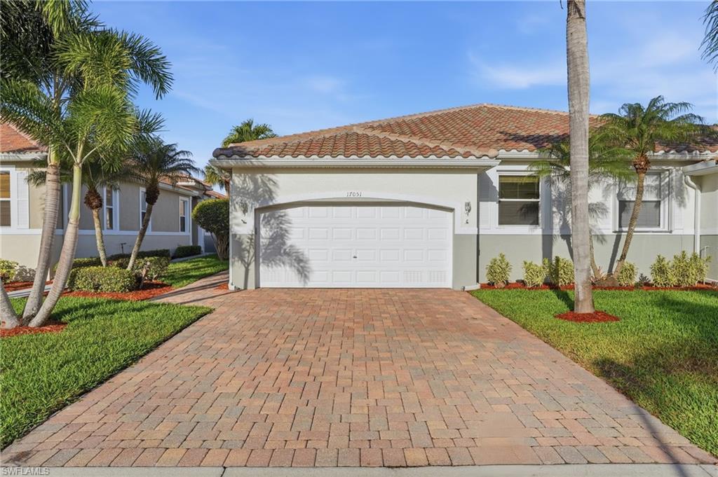 Mediterranean / spanish-style house with decorative driveway, a tiled roof, an attached garage, stucco siding, and a front lawn - Virtually Edited Image
