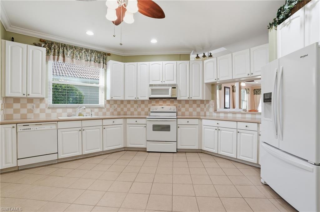 Kitchen featuring white appliances, white cabinetry, a ceiling fan, crown molding, and recessed lighting - Virtually Edited Image