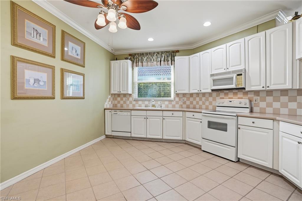 Kitchen with white appliances, white cabinetry, ornamental molding, and a ceiling fan - Virtually Edited Image
