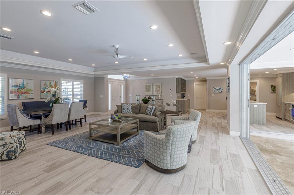 Living room with ceiling fan, a raised ceiling, crown molding, and light wood-type flooring