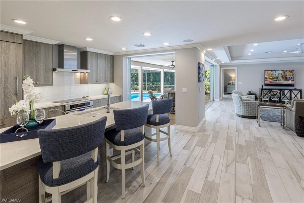 Kitchen featuring ceiling fan, light hardwood / wood-style floors, tasteful backsplash, a raised ceiling, and wall chimney exhaust hood