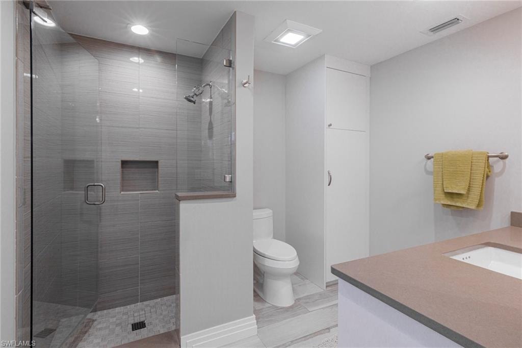 Bathroom with tile floors, a shower with door, vanity, and toilet