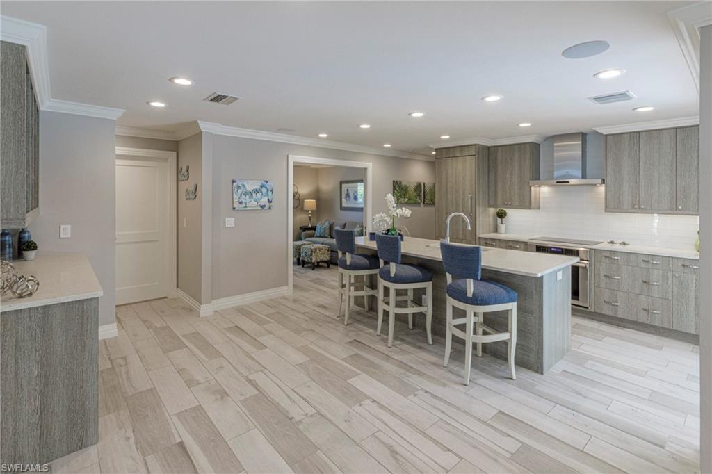 Kitchen featuring light hardwood / wood-style floors, a kitchen breakfast bar, tasteful backsplash, an island with sink, and wall chimney exhaust hood