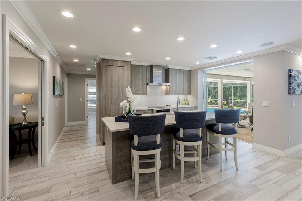 Kitchen with wall chimney range hood, tasteful backsplash, ornamental molding, light wood-type flooring, and a breakfast bar